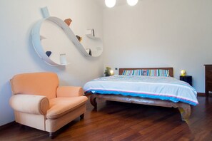 A bedroom with a bed, a chair, a wall-mounted shelf, and a bedside table.