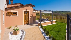A house with a paved entrance, a wooden door, and a small garden area with a lawn and a pergola. - Cozy family-friendly fenced villa, pool and outdoor jacuzzi (Karojba)