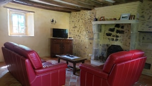 Una sala de estar con un sofá de cuero rojo, un televisor, una chimenea de piedra y una ventana.