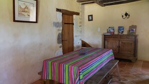 Una habitación con una mesa de madera cubierta por un mantel a rayas, un banco, un armario de madera con libros y un cuadro en la pared.