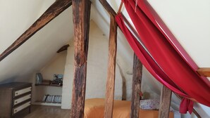 Un dormitorio con techo inclinado, vigas de madera, una cama con ropa de cama naranja y un dosel rojo.