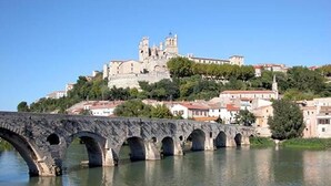 Un pont de pierre enjambe une rivière, et on aperçoit, au loin, sur une colline, un bâtiment historique.