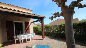 Une terrasse avec une table et des chaises, un espace abrité et un arbre.