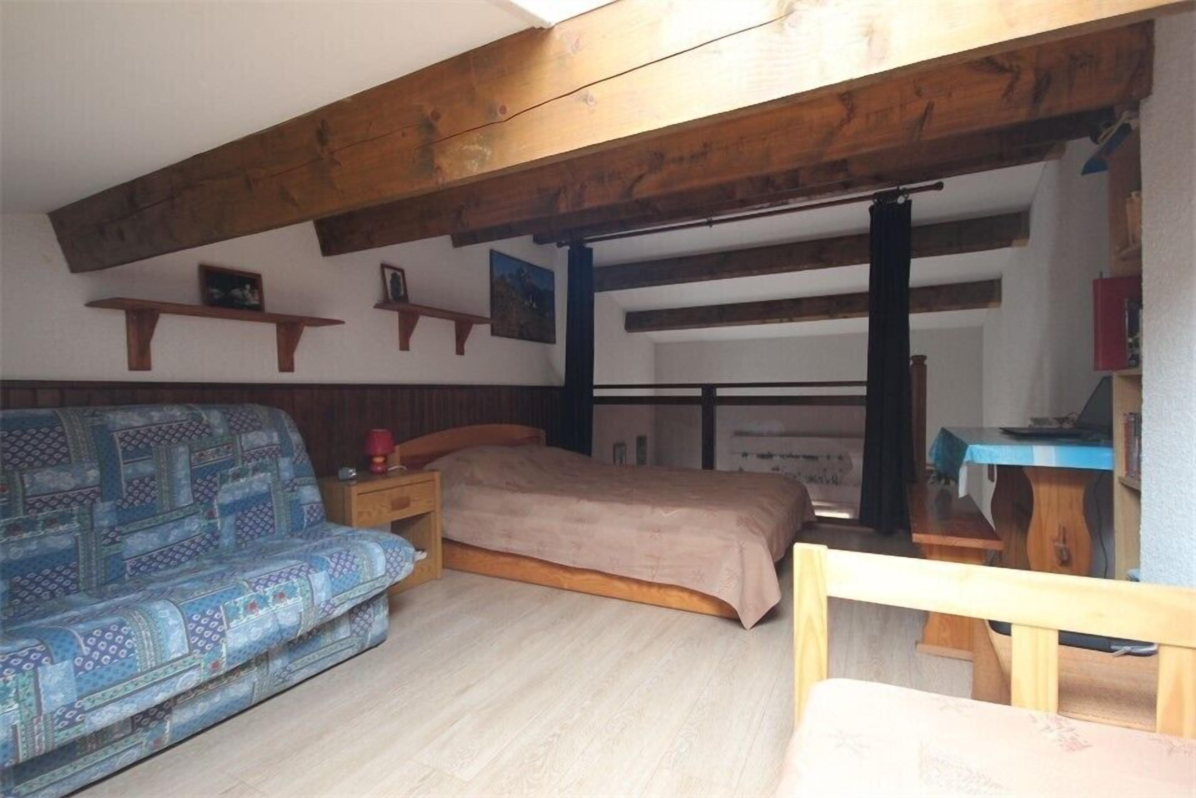 Ein Zimmer mit Bett, einer Couch, Holzbalken, Regalen und einem Schreibtisch.