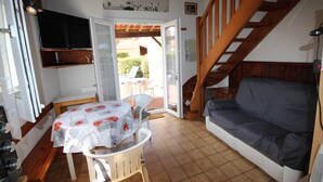 Un salon chaleureux avec un escalier en bois, un coin repas avec une table et des chaises, et un canapé.