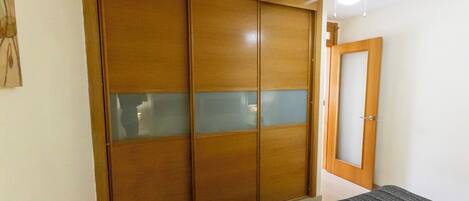 Un dormitorio con un armario de madera, una cama con manta gris y un ventilador de techo.