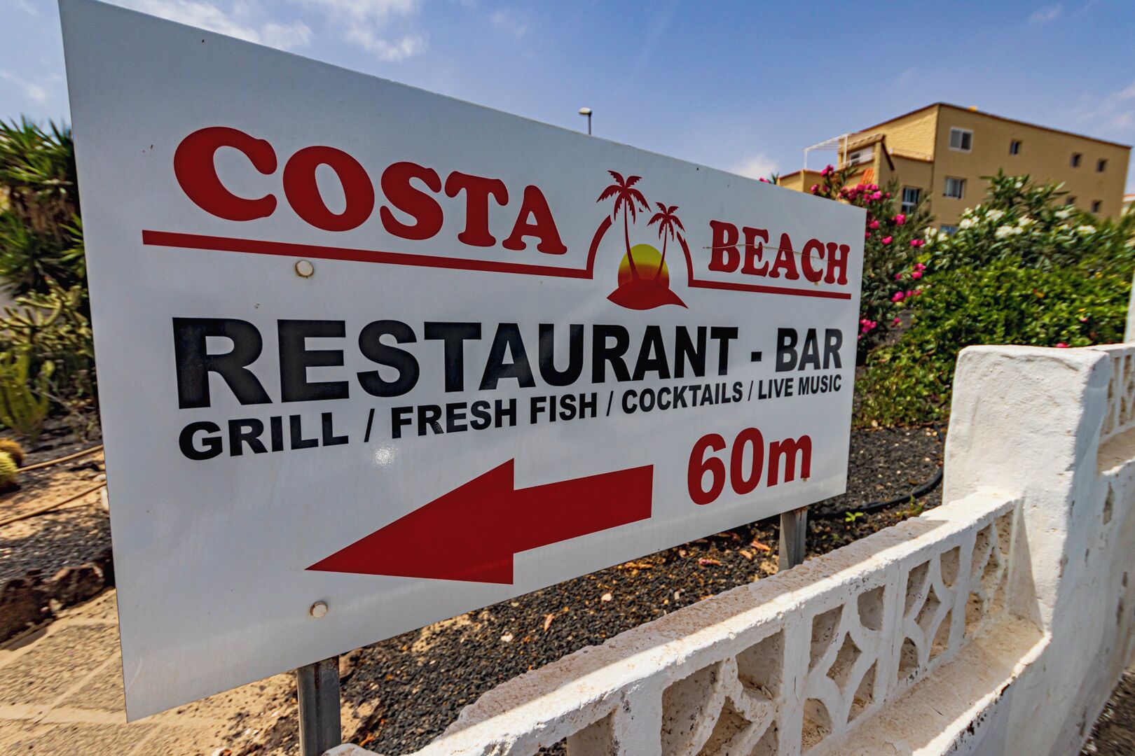 A sign for Costa Beach Restaurant-Bar, indicating it offers a grill, fresh fish, cocktails, and live music.