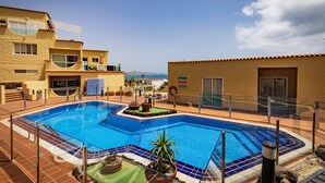 Un espace piscine offrant une vue dégagée sur la mer, un bâtiment doté d’un toit en tuiles et un drapeau.