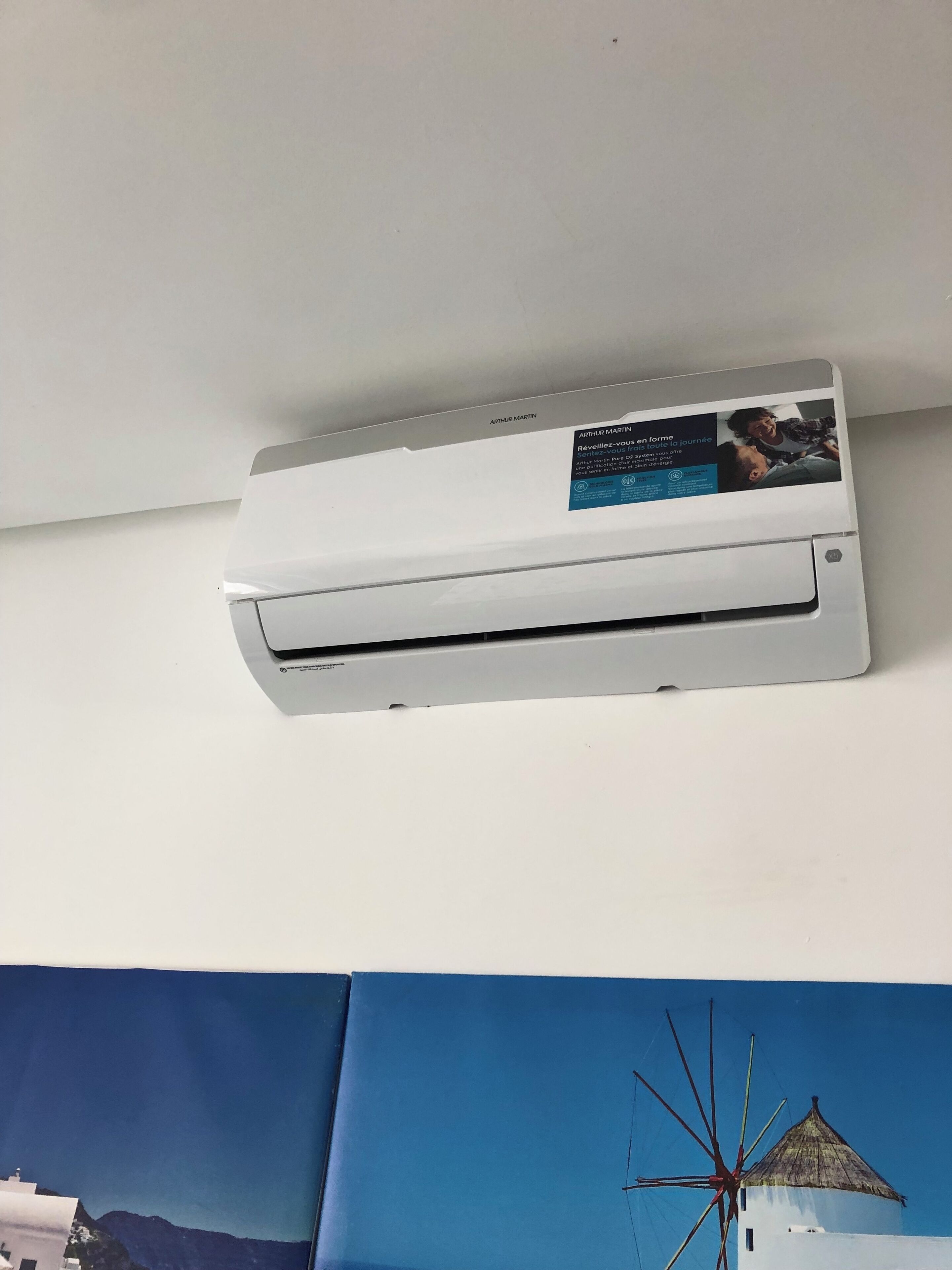 A white air conditioning unit mounted on a wall with a sticker advertising Arthur Martin.