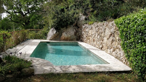 A rectangular swimming pool with stone tiles, surrounded by greenery and a rocky wall. - Independent studio in villa overlooking Monaco + parking in Monaco (beausoleil)