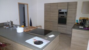 Une cuisine moderne dotée d’un four encastré, d’un four à micro-ondes et d’un grand îlot central muni d’une planche à découper et d’une bouilloire.