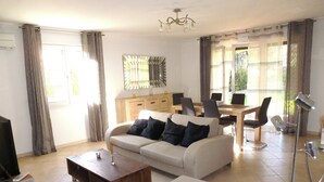 Un salon comprenant un canapé, une table basse, un téléviseur et un coin repas avec des chaises et une table.