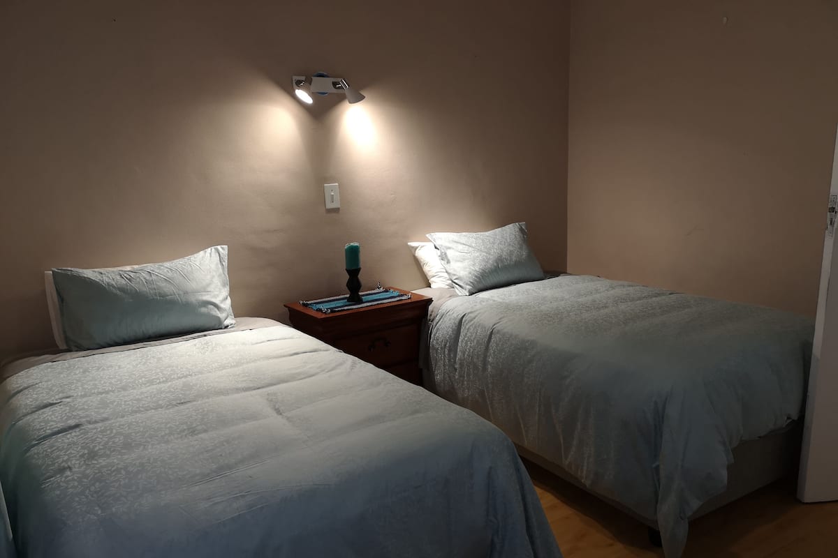 A bedroom with two single beds, a nightstand with a lamp, and a wall-mounted light fixture.