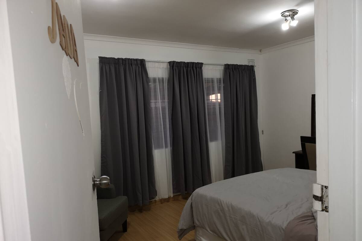 A bedroom with a bed, a bedside table, a chair, and a window with curtains.