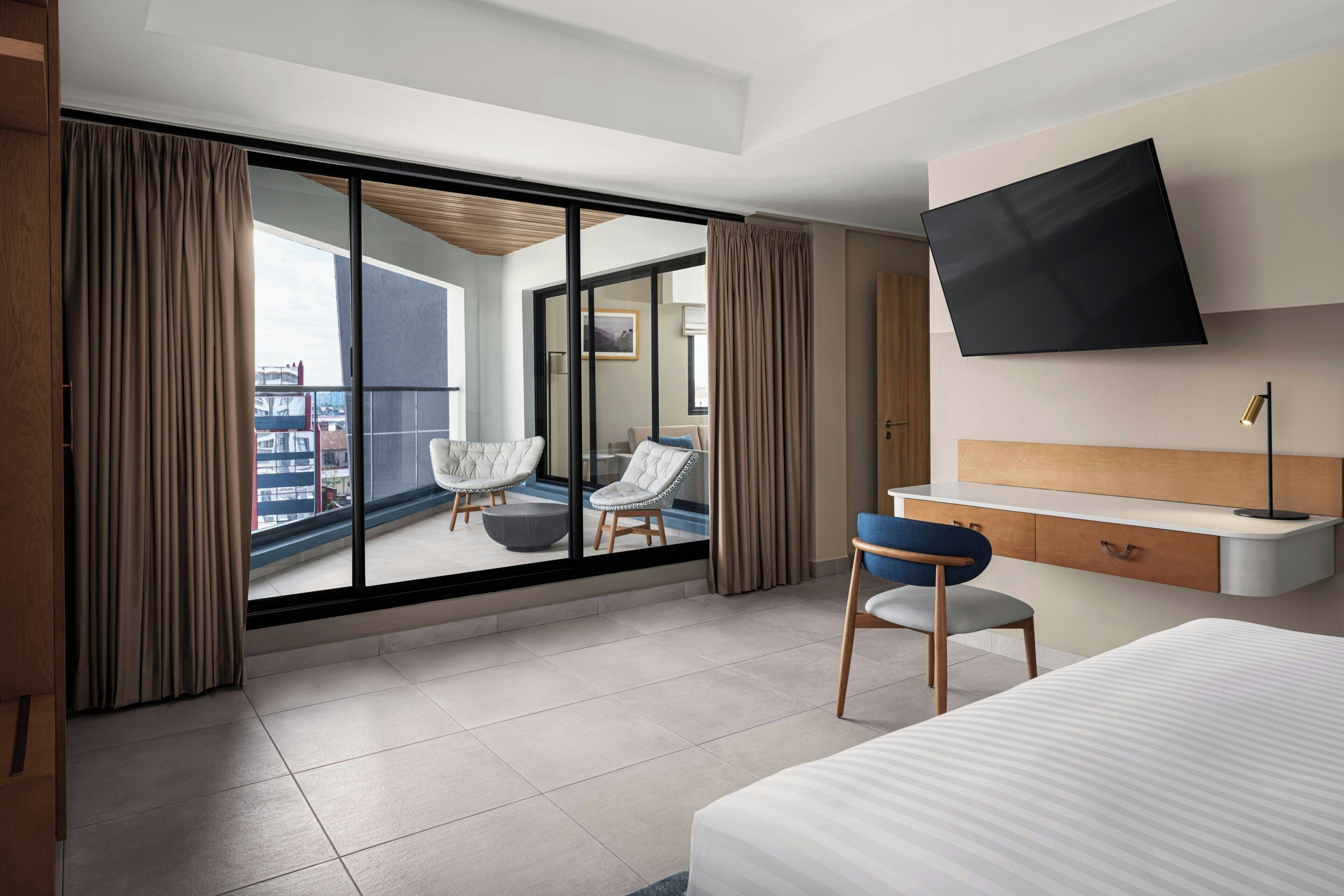 Een moderne hotelkamer met een groot raam, een flatscreen televisie, een bureau met een stoel en een bed.