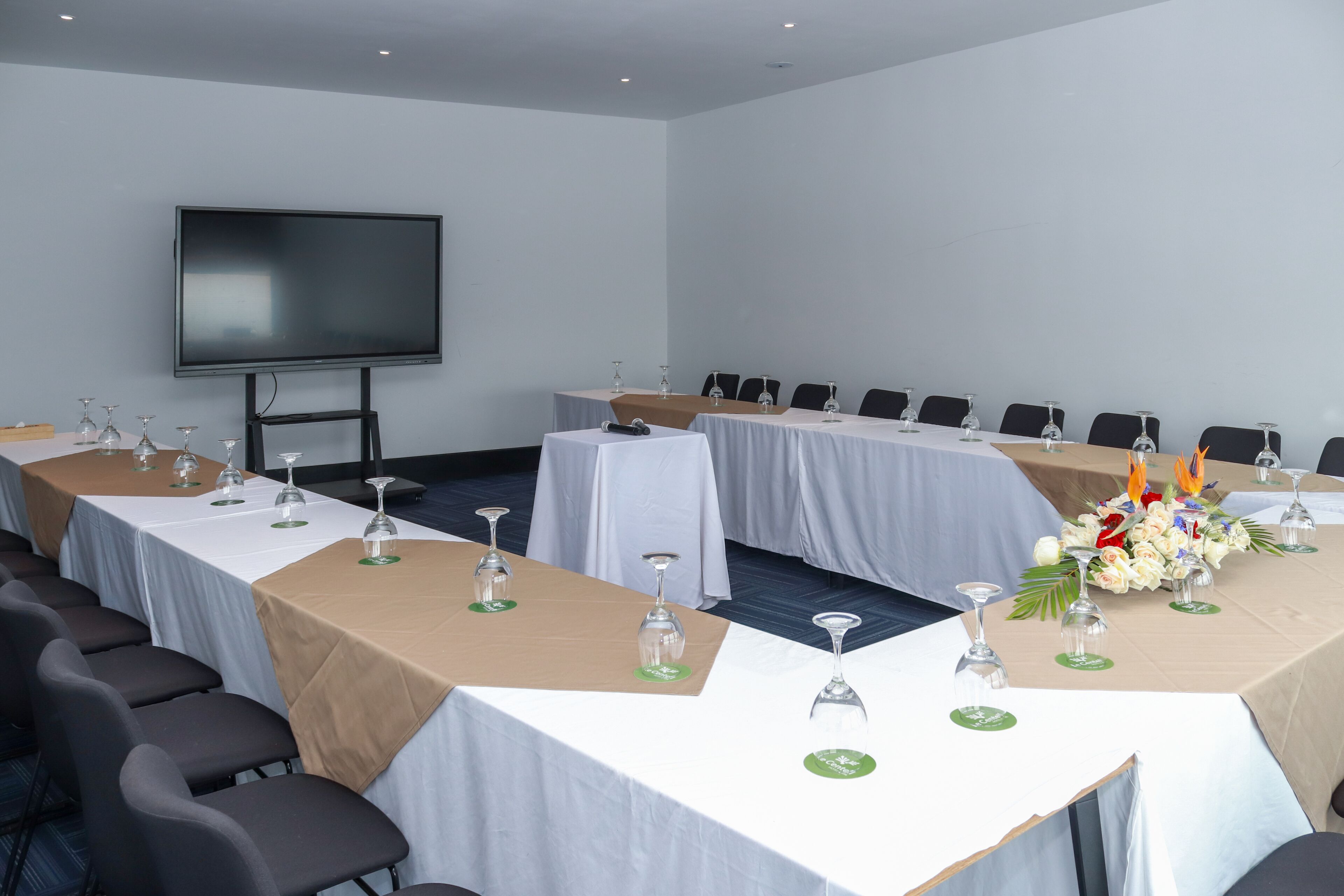 A conference room with multiple tables, each set with wine glasses and water bottles, and a large screen on the wall.