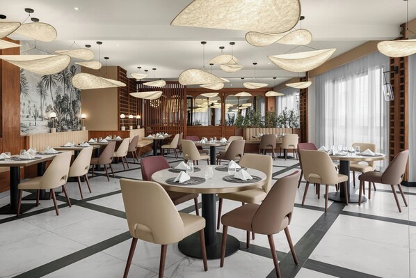 A modern restaurant with round tables, beige chairs, and unique hanging light fixtures.