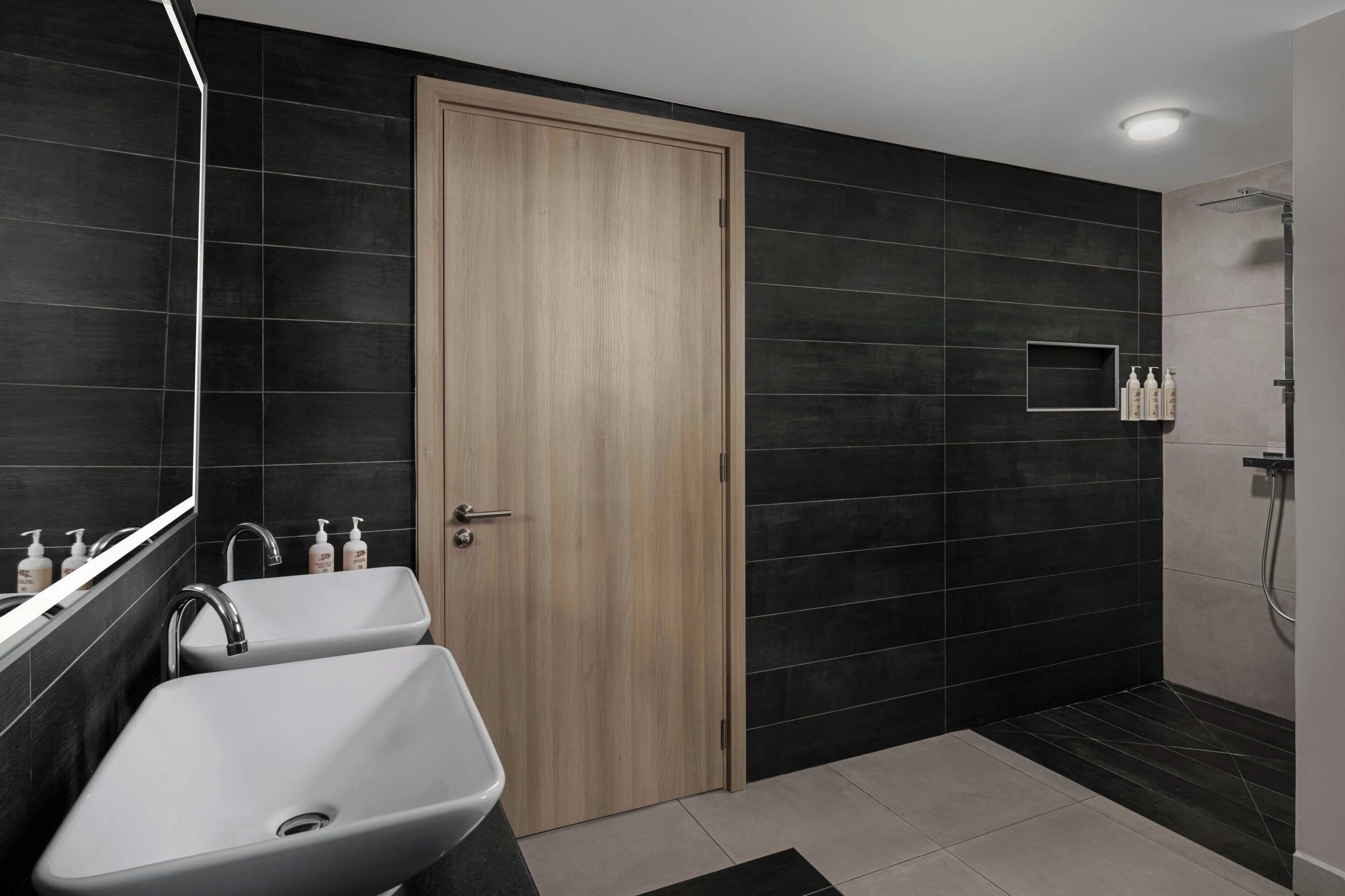 Un baño moderno con dos lavamanos, una puerta de madera y una zona de ducha.