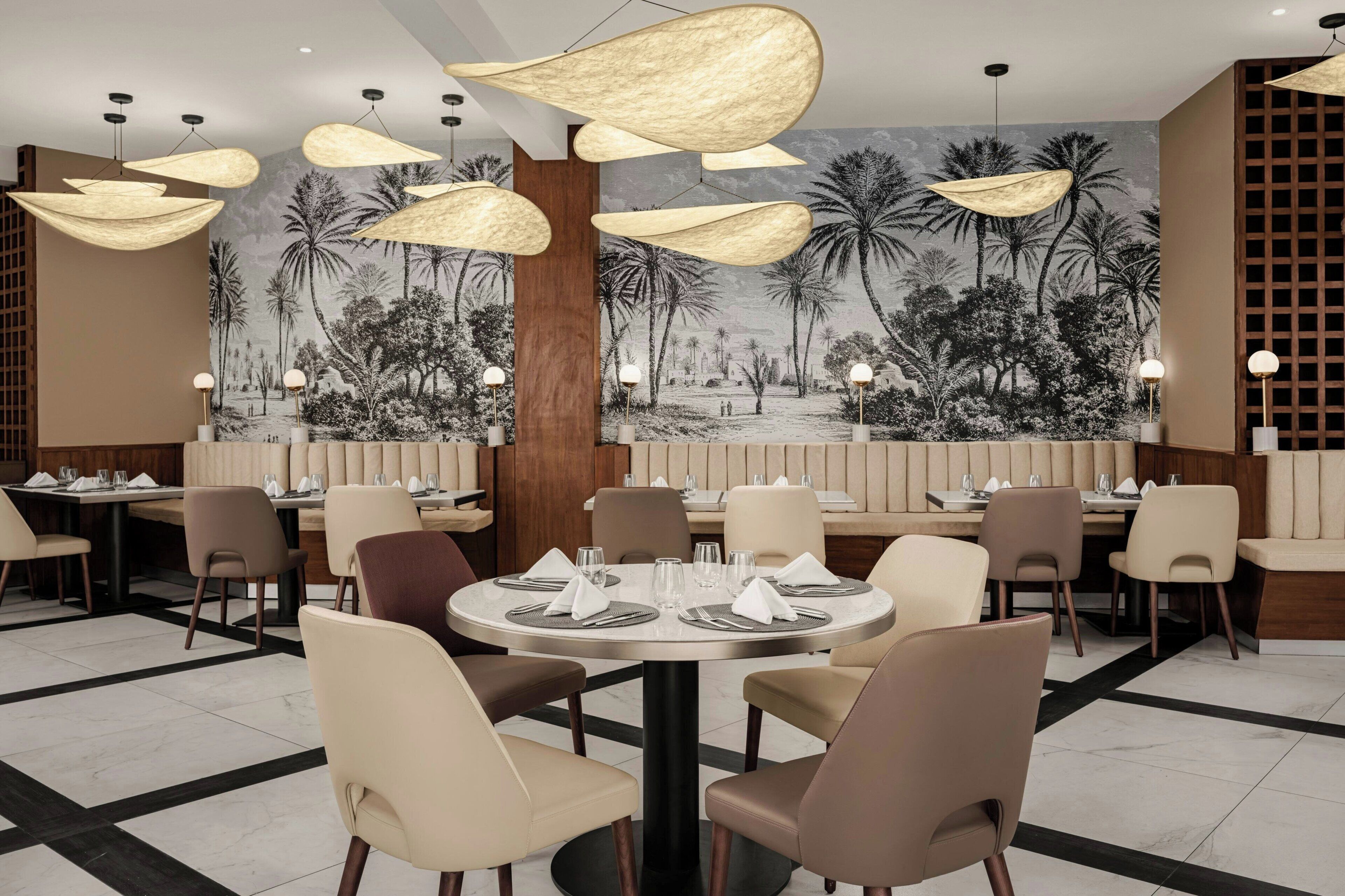 Um restaurante com mesas redondas, cadeiras e luminárias pendentes.