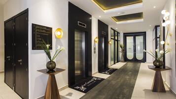 Un moderno vestíbulo de hotel con mostrador de recepción, decoración en blanco y negro, y un plano que indica servicios como estacionamiento, restaurante, spa, gimnasio y salas de reuniones.