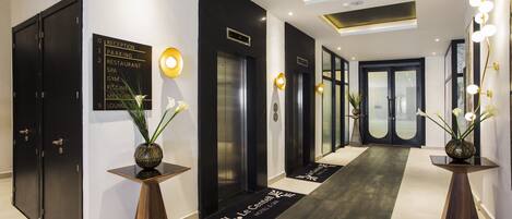 Un moderno vestíbulo de hotel con mostrador de recepción, decoración en blanco y negro, y un plano que indica servicios como estacionamiento, restaurante, spa, gimnasio y salas de reuniones.