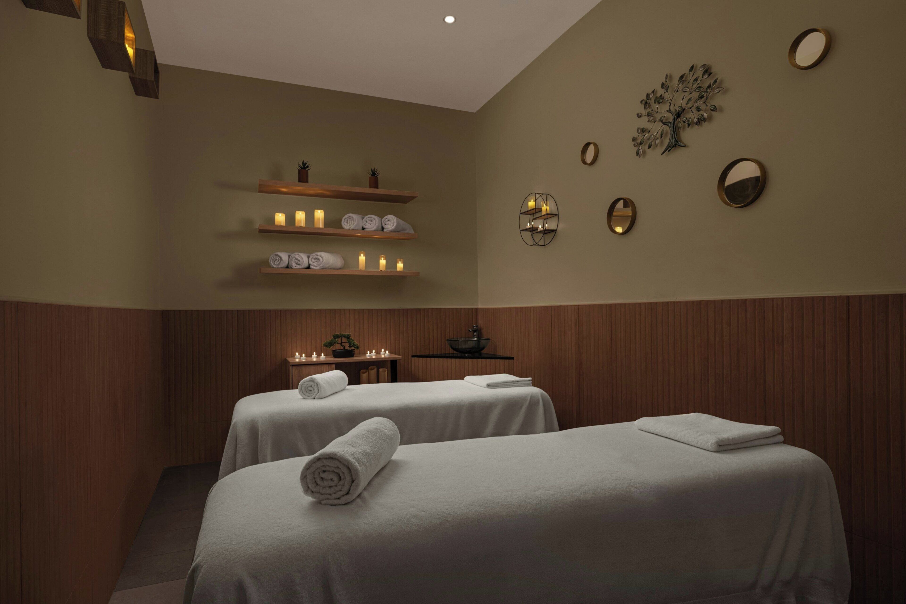 Un cuarto de spa con dos camas, paneles de madera y repisas con velas y toallas.