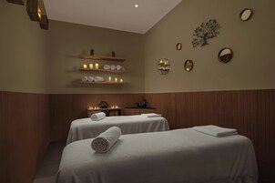 Un cuarto de spa con dos camas, paneles de madera y repisas con velas y toallas.