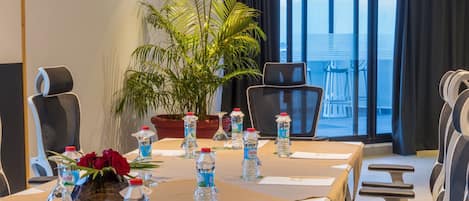 A conference room with a long table, chairs, water bottles, a vase with red flowers, and a potted plant.