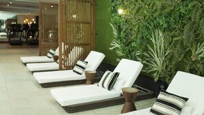 Uma área de spa com cadeiras de descanso, uma parede verde com plantas e um painel de madeira.