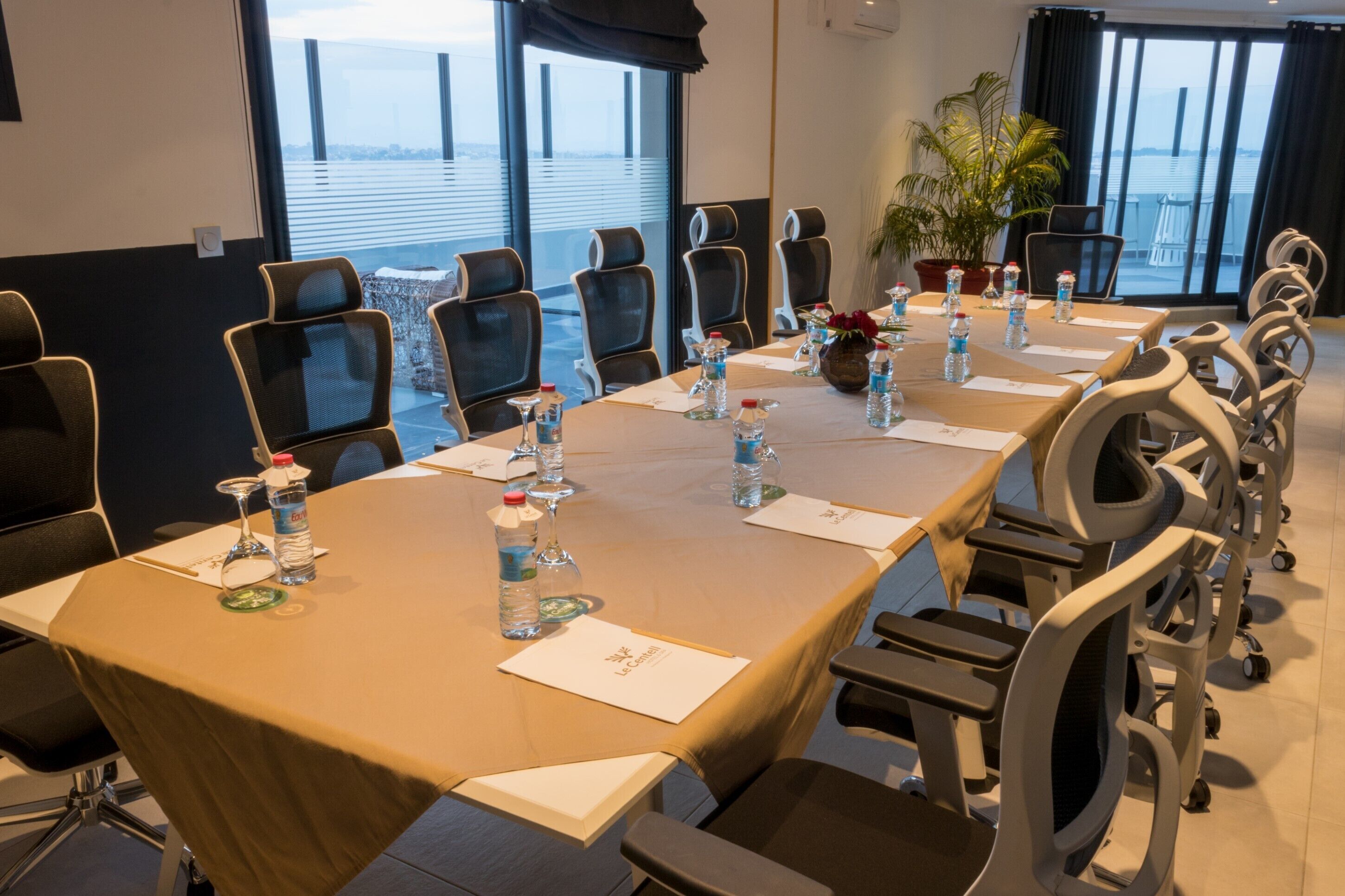 A conference room with a long table, chairs, water bottles, and a potted plant.
