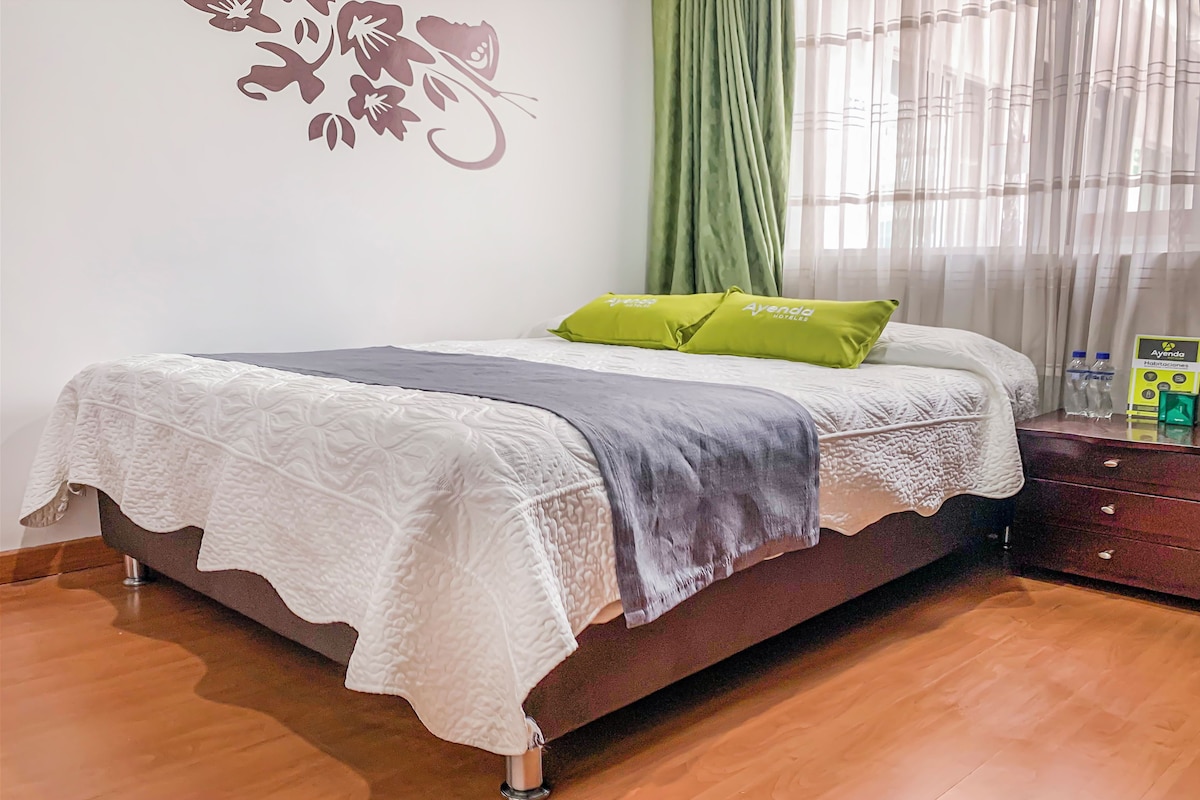 A neatly made bed with a white and gray blanket, a green pillow, and a decorative wall piece.