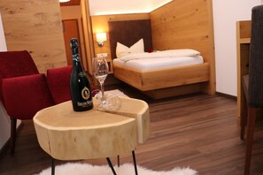 A cozy room with a wooden bed, a red chair, a small wooden table with a bottle and glass, and a fluffy rug. - Gasthof-Pension Kerber (Fürstenstein)