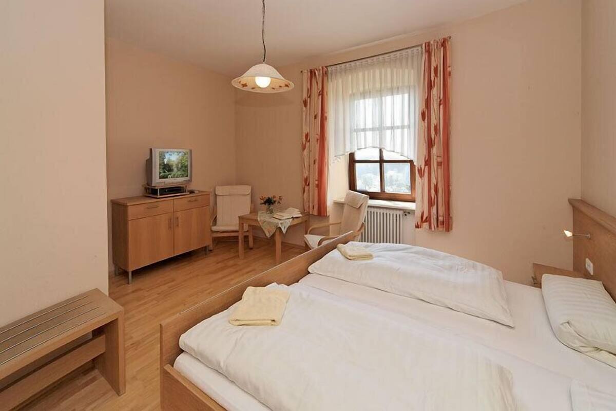 Une chambre d’hôtel avec deux lits, un bureau avec une télévision, une chaise et une fenêtre avec des rideaux.