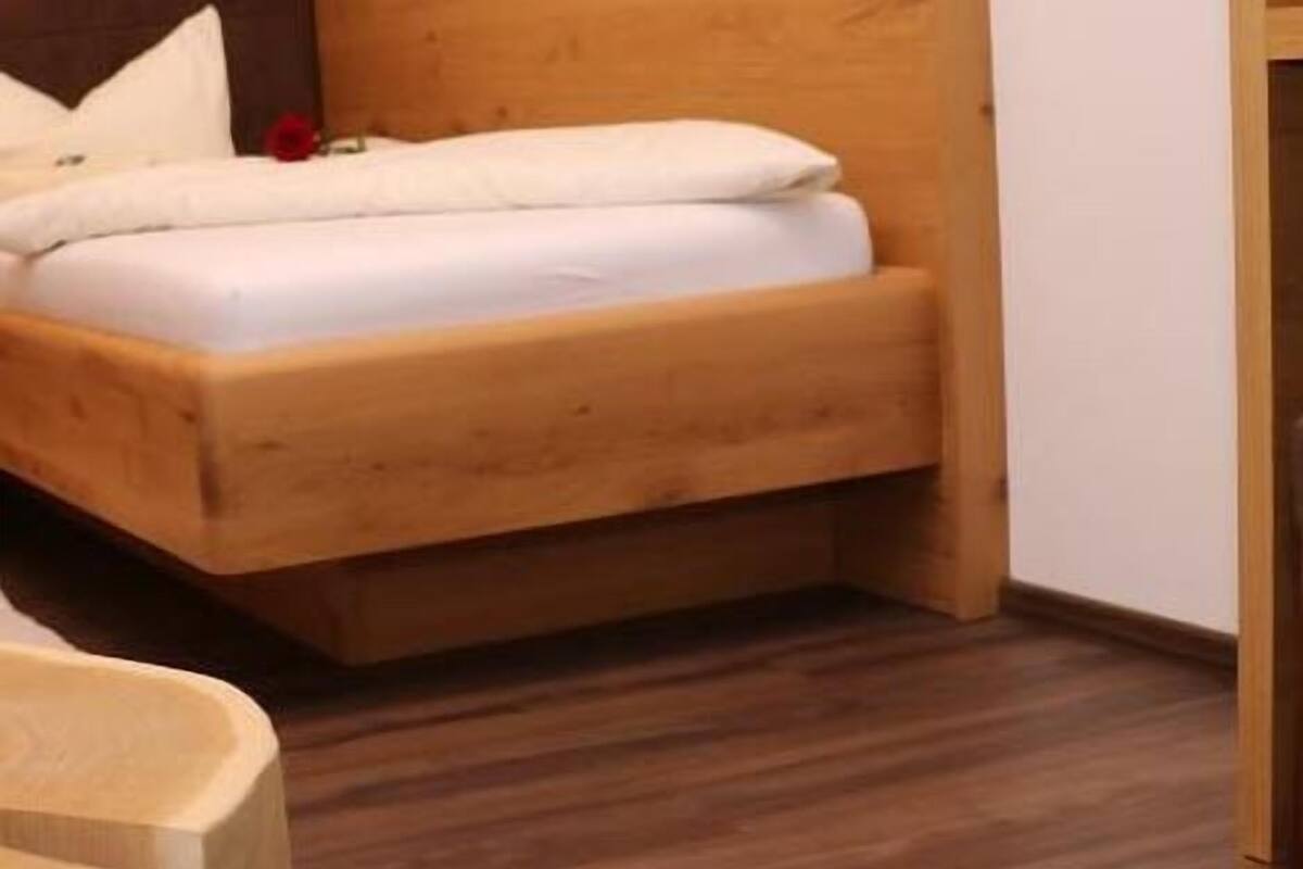 Un lit en bois dans une pièce dont le sol est en bois et dont un des murs est blanc.