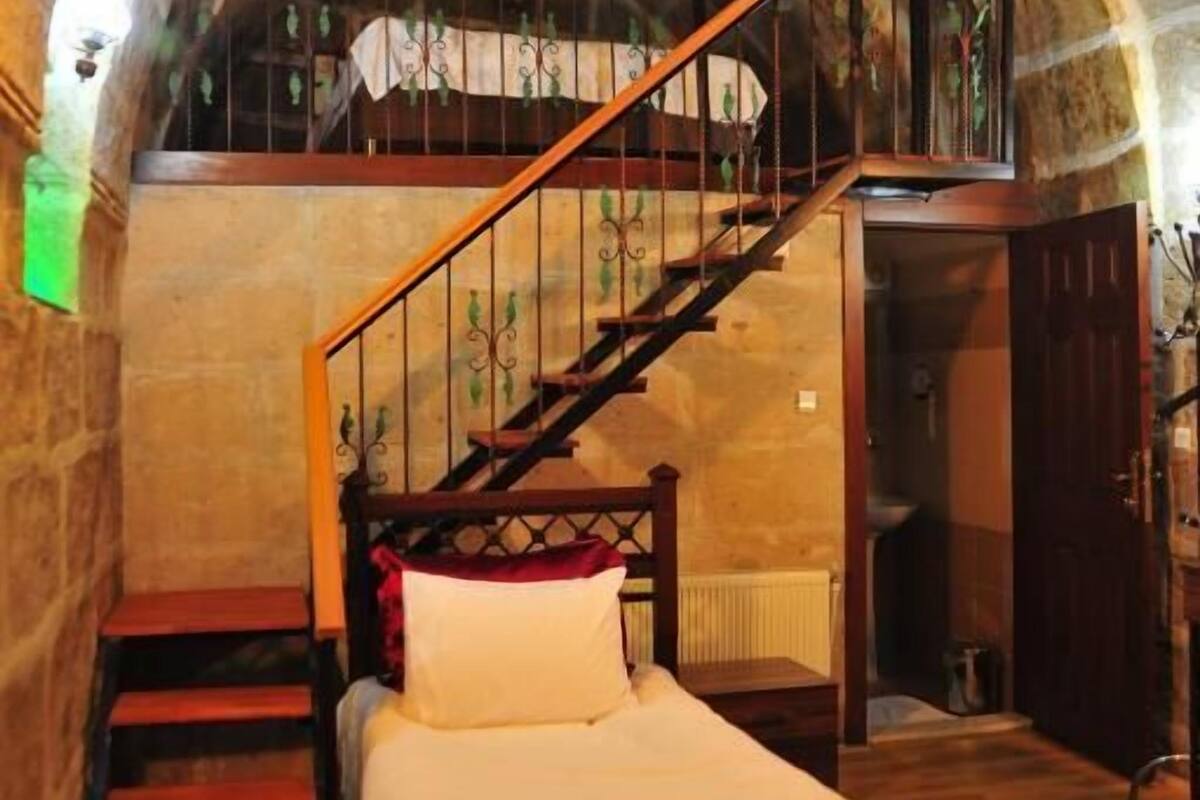 Un dormitorio con una cama de madera, una escalera que sube a un nivel superior y una pared de piedra.