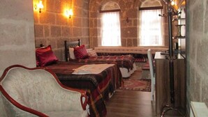 Una habitación con paredes de piedra, una cama de madera, un banco y un escritorio con lámpara.