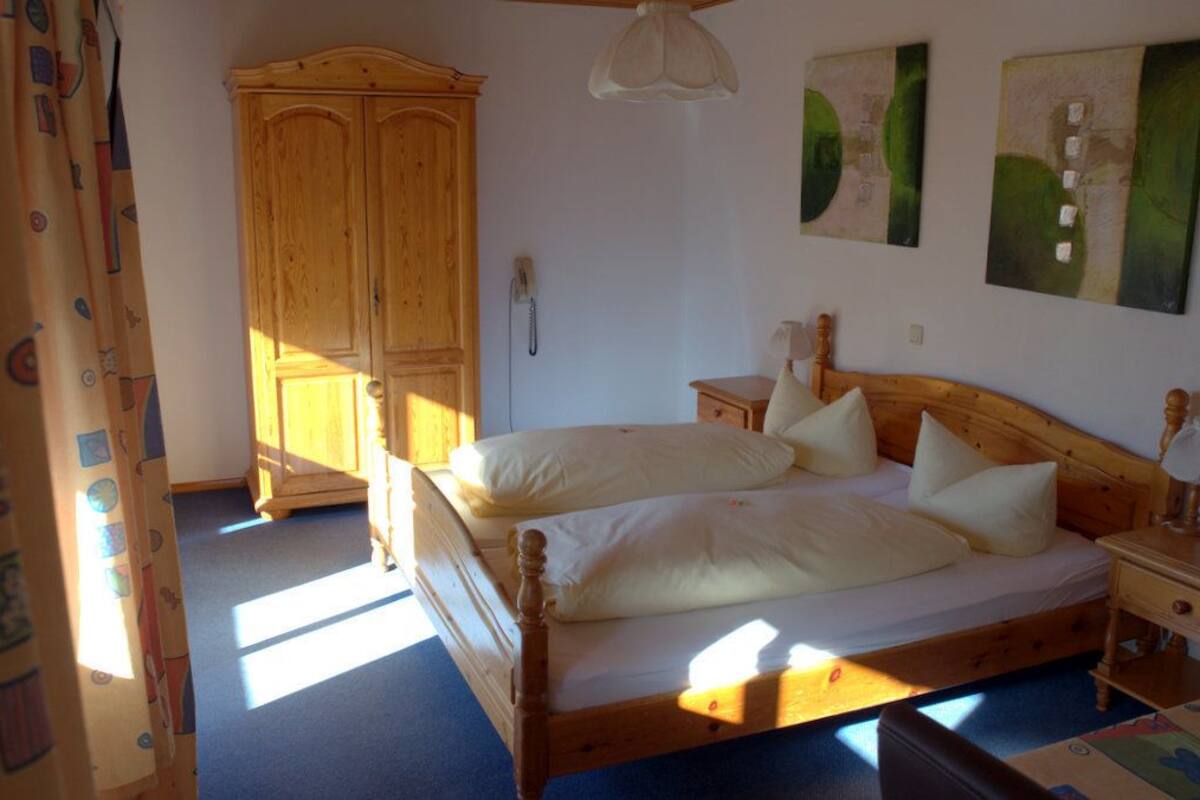 A bedroom with a double bed, a wooden wardrobe, a bedside table with a lamp, and a ceiling fan.