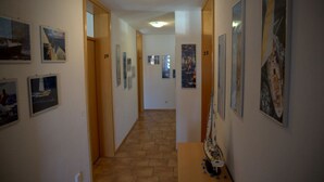 A hallway with numbered doors, artwork on the walls, and a tiled floor. - Pension Aufeld (Landsberg am Lech)
