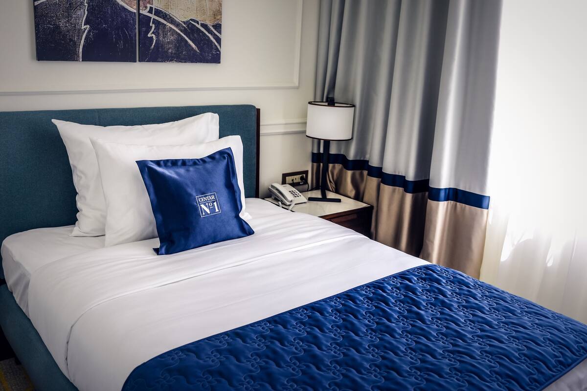 A hotel room with a bed, a nightstand, a lamp, and curtains.