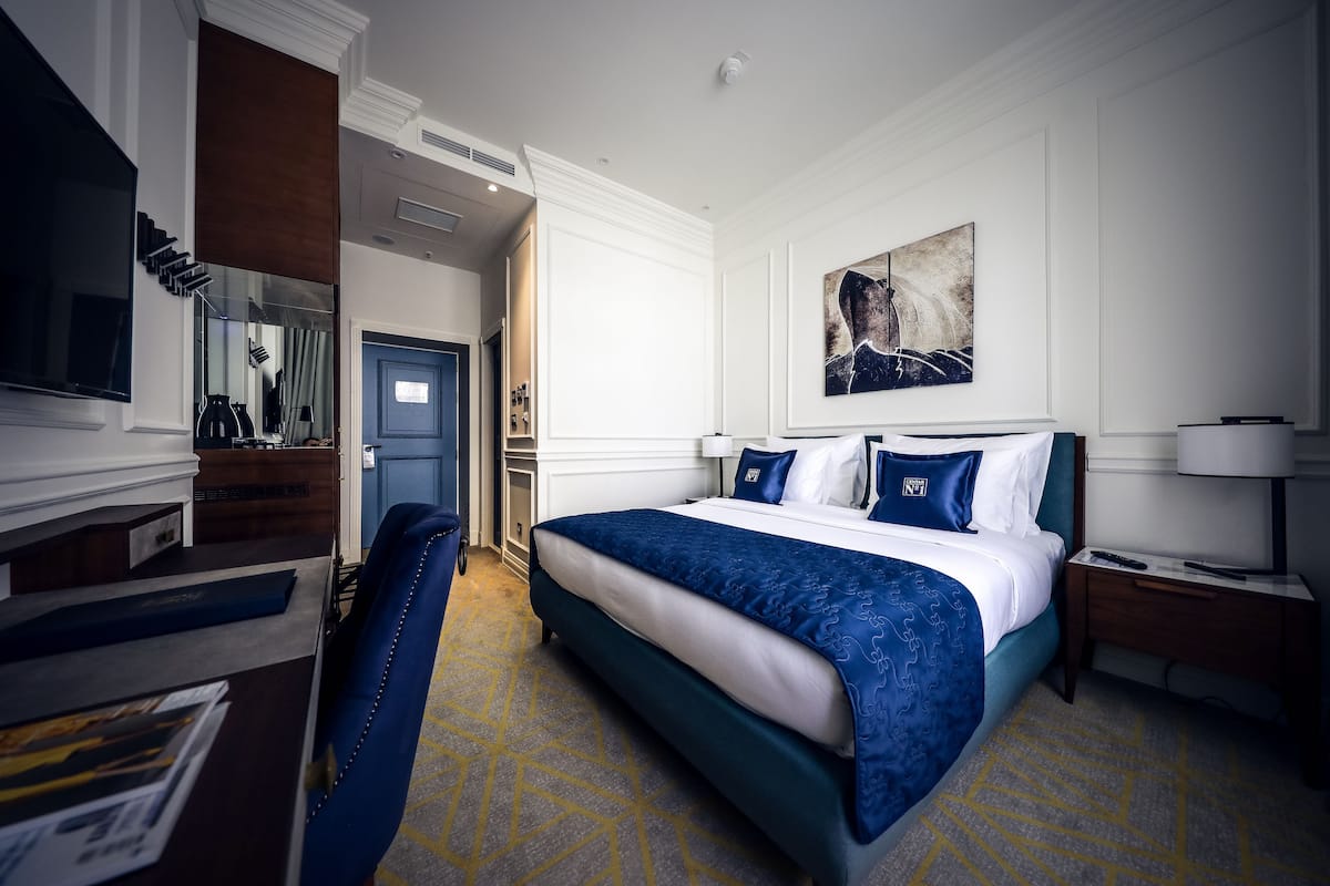 A hotel room with a large bed, a desk with a chair, a TV, and a painting on the wall.
