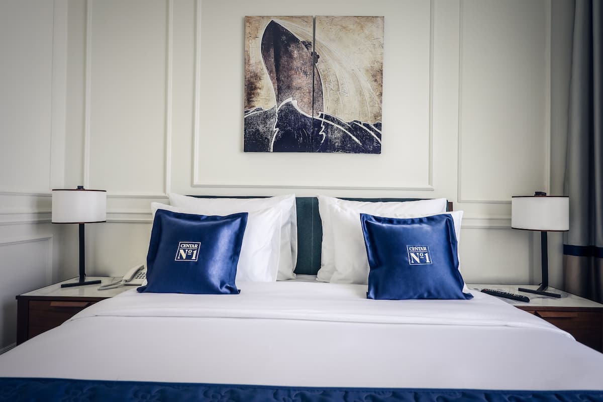 A hotel room with a large bed, two nightstands, a telephone, and a wall-mounted artwork.