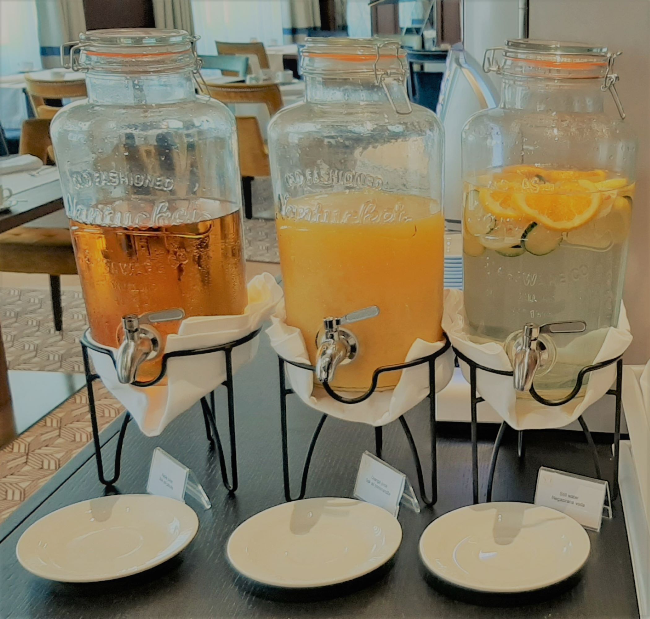 Three glass dispensers with different beverages on a table in a cafe setting.