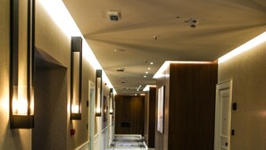 Un pasillo de hotel con alfombra estampada, luces empotradas en la pared y puertas a ambos lados.