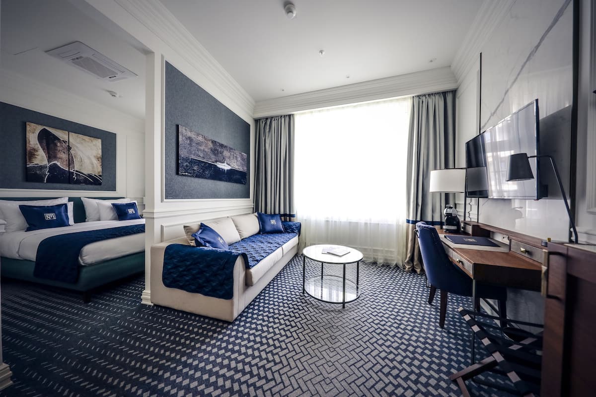 A hotel room with a bed, sofa, desk, and TV.