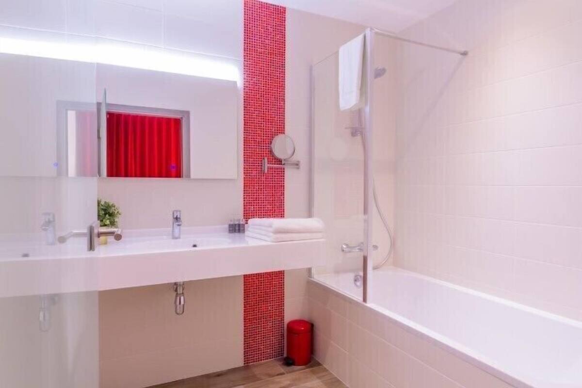 Un baño moderno con un lavamanos blanco, cabina de ducha con mampara de cristal y una pared de acento roja.