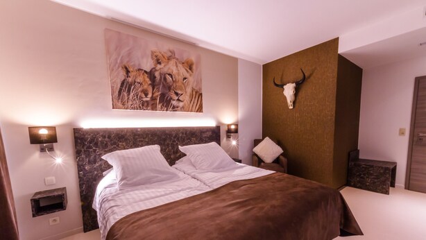 A modern bedroom with a large bed, a headboard with a lion painting, a wall-mounted skull, and bedside lamps. - ManavaHotel (Herstal)