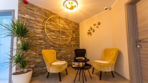 A corner room with a stone wall, two yellow chairs, a small table, and a potted plant. - ManavaHotel (Herstal)