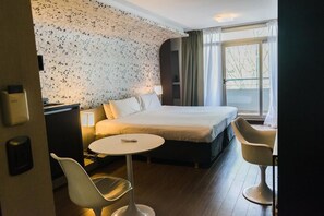 Een hotelkamer met een groot bed, een bureau met lamp, een klein rond tafeltje en twee stoelen.