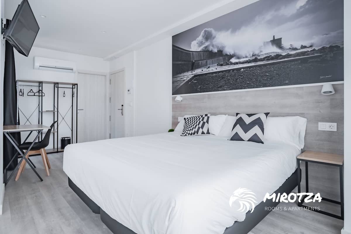 A modern hotel room with a large bed, a desk, and a chair. There is a painting of a stormy sea on the wall.