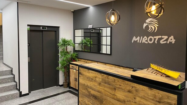 A modern reception area with a wooden counter, a digital display, and a mirror. - Mirotza Rooms (Orio)